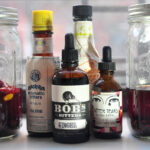 2 jars of homemade bitters with several bottles of store-bought bitters in the middle