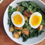 Kale Caesar salad with a two halves of a soft boiled egg on top