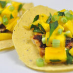 chipotle glazed tilapia tacos topped with mango and cilantro on a white plate