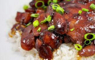 Chicken Adobo over a pile of white rice on a white background with scallions sprinkled on top