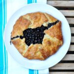 blueberry crostata on a white plate with blue striped dish towel