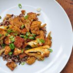 white plate with gochujang tofu and cauliflower on a bed of rice