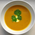 bowl of butternut squash soup with drizzle of sour cream and cilantro leaves