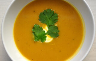 bowl of butternut squash soup with drizzle of sour cream and cilantro leaves