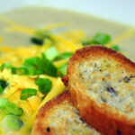 cauliflower soup topped with cheddar and scallions with sliced baguette