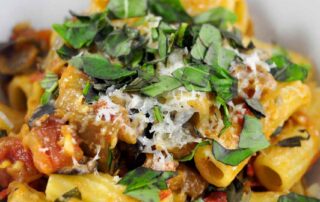 eggplant tomato pasta piled in a bowl and topped with cheese and basil