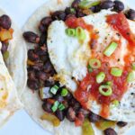 tortillas topped with beans, a fried egg, salsa and scallions