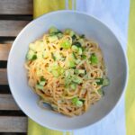 white bowl with sesame noodles topped with cucumbers and scallions