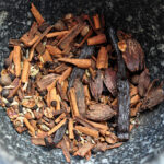 a mortar with broken up spices and a vanilla bean