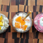 whipped cream with mango, oranges and raspberries in cups with gold spoons