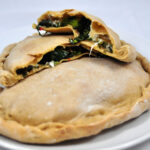 broccoli rabe calzone cut in half laying on top of another calzone