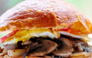 Close up of bun with fried egg, mushroom hash and a glimpse of tomato