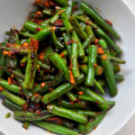 green beans covered in chile paste, garlic and soy sauce piled into a white bowl