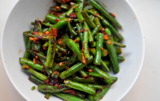 green beans covered in chile paste, garlic and soy sauce piled into a white bowl