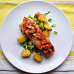 white plate with pile of roasted potatoes and scallions and a fillet of salmon glazed with soy and garlic and topped with kimchi