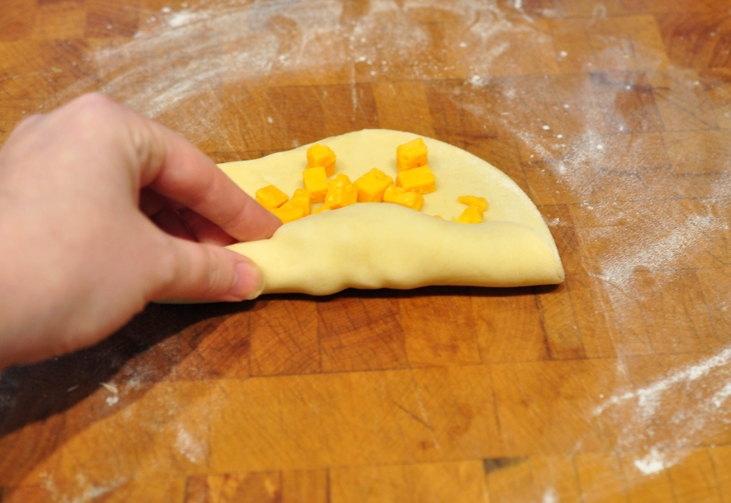 piece of dough on wooden counter with cheese layered on it being rolled up into a log