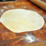 rolled out roti on a countertop with rolling pin in background