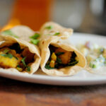 Potato and kale rolled up in a roti with raita on the side and cilantro sprinkled on top.