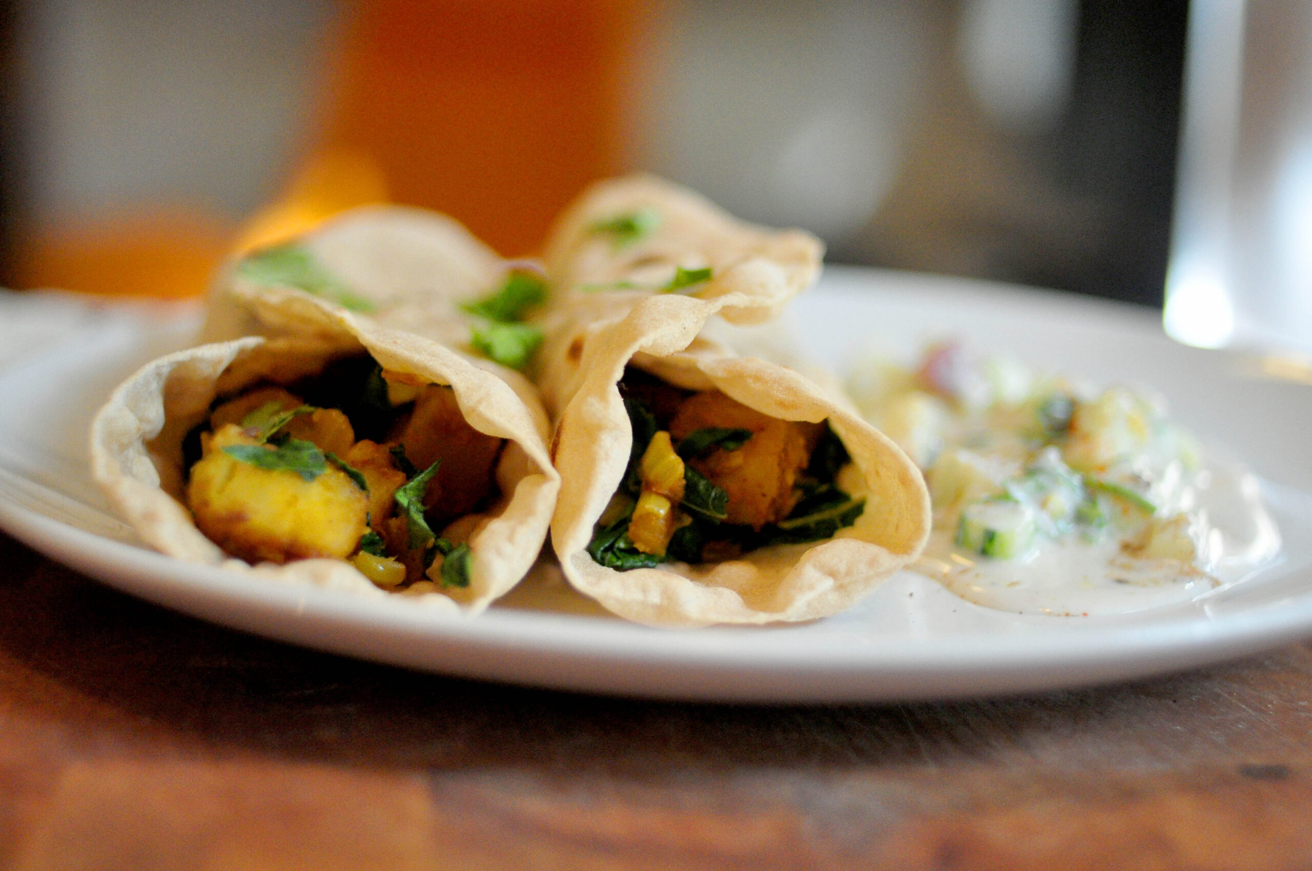 Potato and kale rolled up in a roti with raita on the side and cilantro sprinkled on top.