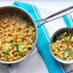 welsh rarebit macaroni and cheese with broccoli in a pot on a teal striped tea towel and in a bowl with a fork