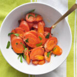 roasted sliced carrots with ginger and butter piled in a white bowl with a light green and white cloth underneath