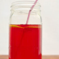 jar of bright pink agua fresca with lemon slices floating in it and a straw