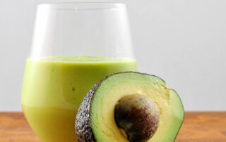 avocado milkshake in glass with half an avocado leaning on it