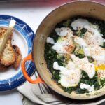 orange pot with green shakshuka in it and a plate with toast and a butter knife