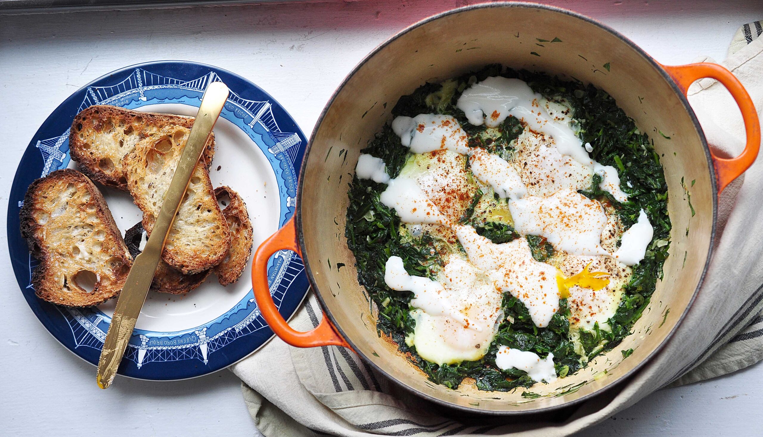 orange pot with green shakshuka in it and a plate with toast and a butter knife