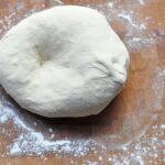raw pizza dough on a wooden board with flour sprinkled around