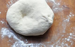 raw pizza dough on a wooden board with flour sprinkled around