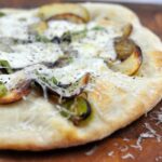 side view of potato and leek pizza on a wooden board