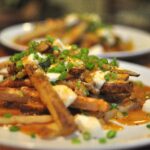 poutine! oven baked fries smothered in gravy, mozzarella and scallions on a white plate
