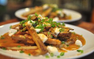 poutine! oven baked fries smothered in gravy, mozzarella and scallions on a white plate