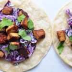two tofu and peanut cabbage slaw tacos on a white background