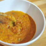 white bowl filled with peanut sauce and a green vegetable dipping into it